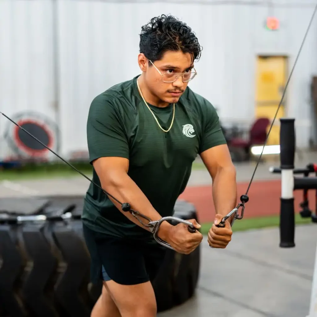 Unconscious Faith fitness model in the gym doing cable flys wearing a green shirt and glasses
