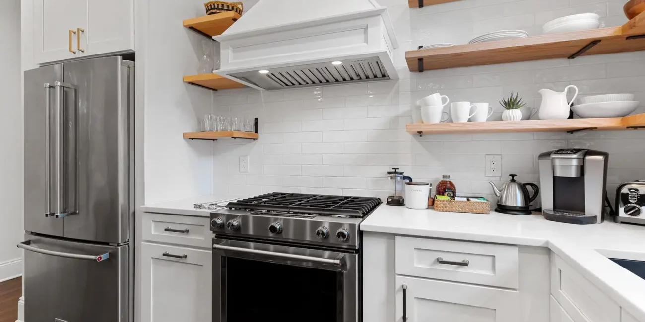 Modern kitchen featuring stainless steel appliances, including a fridge and stove. White cabinets and open wooden shelves add a clean, organized look.