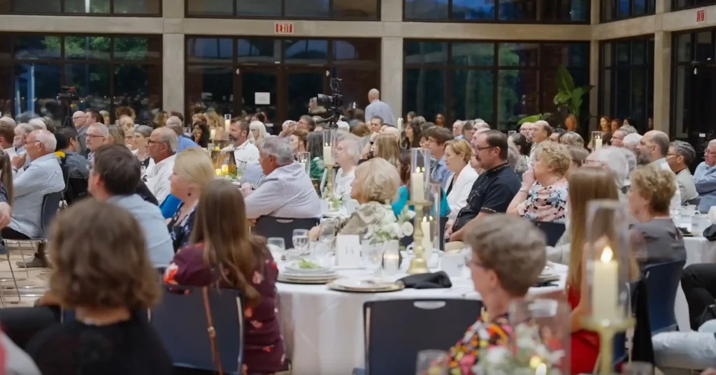 Banquet room at a gala dinner, guests seated at round tables under warm light