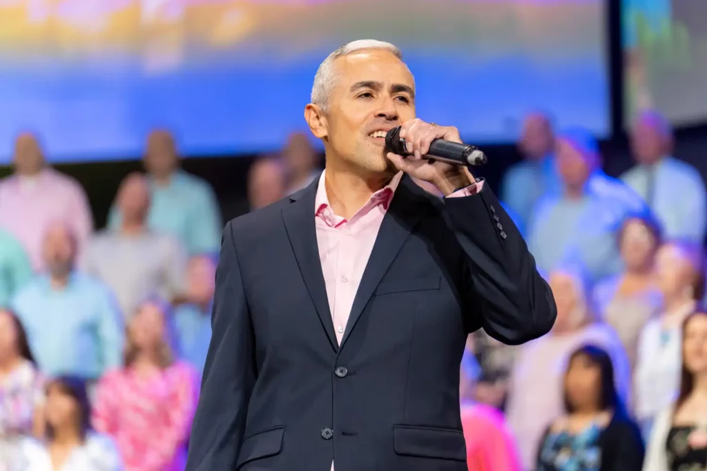 Corporate Event Photography & Videography 5 Presenter in a dark suit speaking into a handheld microphone with the audience filling the frame behind