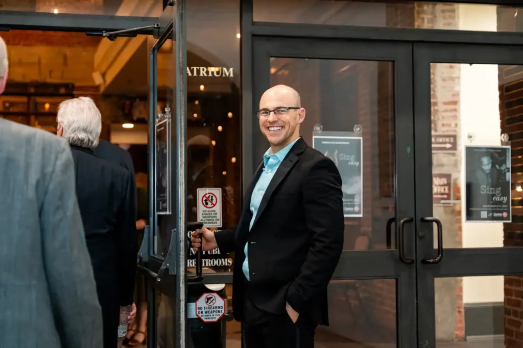 Corporate Event Photography & Videography 14 Host greeting arriving guests at the glass doors of the venue entrance