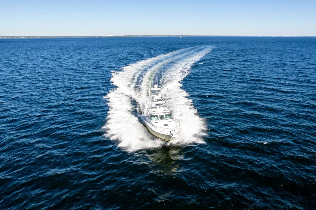 Aerial of a sportfishing yacht running away from the camera, throwing a long white wake across open water