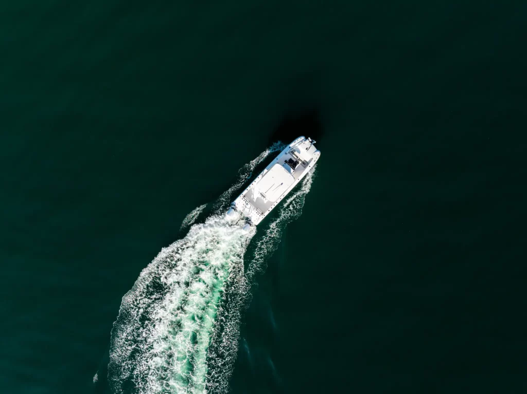 Very high aerial of a Twin Vee power catamaran carving a turn, wake bright against dark green water