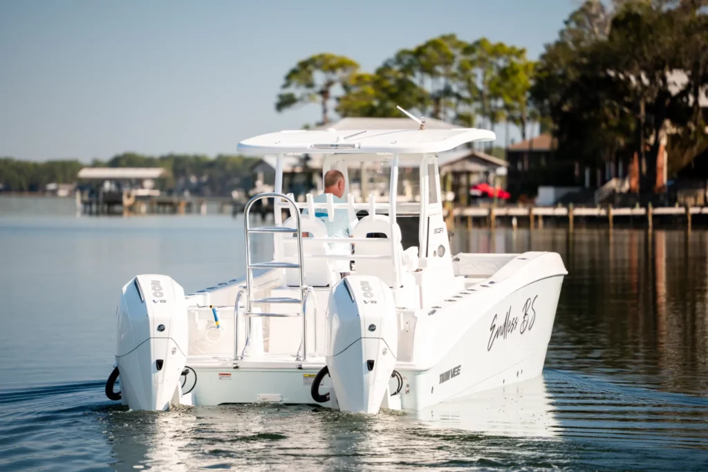 Twin Vee catamaran idling off a wooded shoreline with boathouses behind