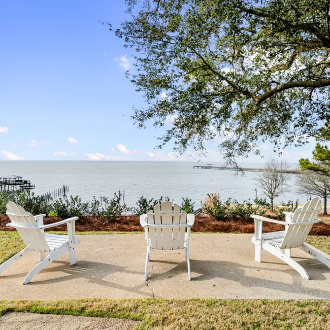 White Adirondack chairs on a patio overlooking Mobile Bay at Emma's Bayhouse, Fairhope