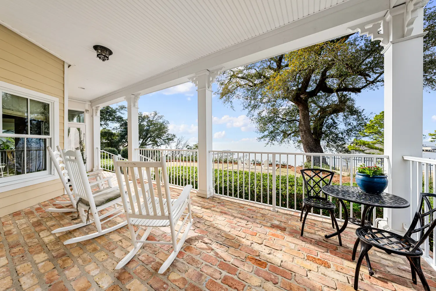 Brick porch with white rocking chairs and bay views under live oaks at Emma's Bayhouse