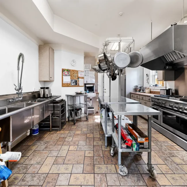 Commercial kitchen with a stainless range, hood and prep tables at Emma's Bayhouse in Fairhope