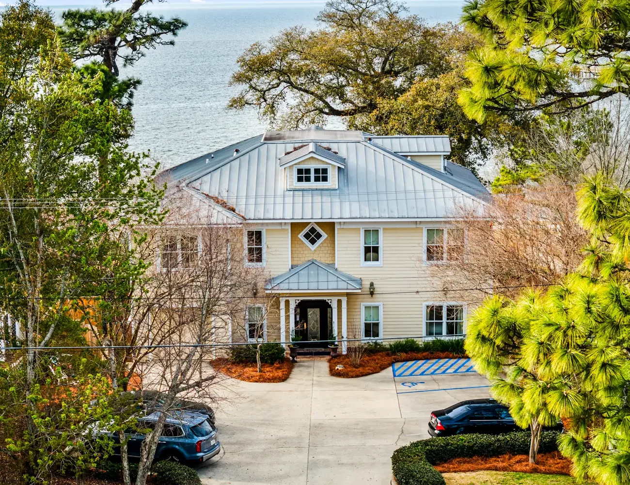 Aerial view of Emma's Bayhouse in Fairhope, Alabama, a bed and breakfast with a metal roof, with Mobile Bay behind it