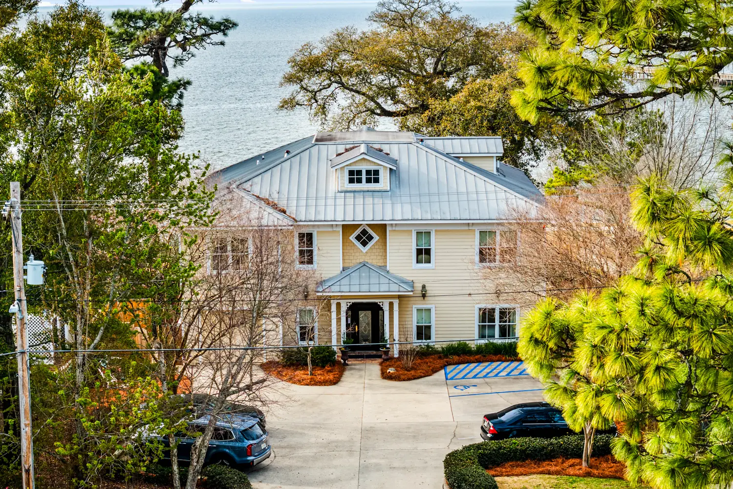 Aerial view of Emma's Bayhouse in Fairhope, Alabama, a bed and breakfast with a metal roof, with Mobile Bay behind it