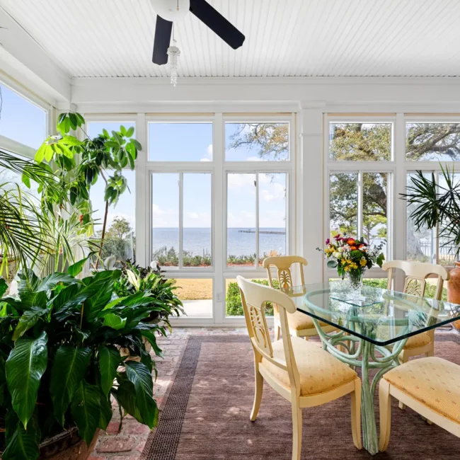 Glass-walled sunroom with a dining table and plants looking out over Mobile Bay at Emma's Bayhouse