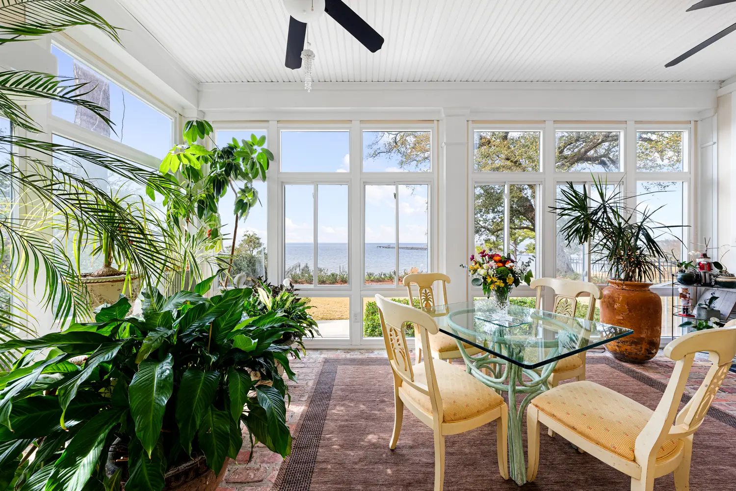 Glass-walled sunroom with a dining table and plants looking out over Mobile Bay at Emma's Bayhouse