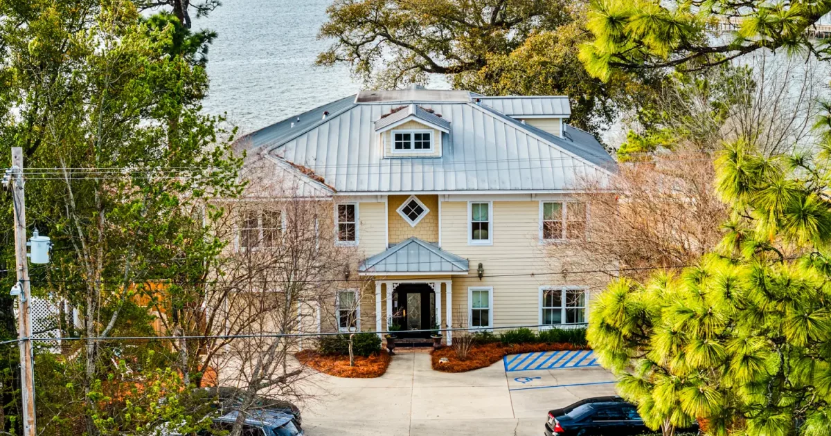 Aerial view of Emma's Bayhouse in Fairhope, Alabama, a bed and breakfast with a metal roof, with Mobile Bay behind it